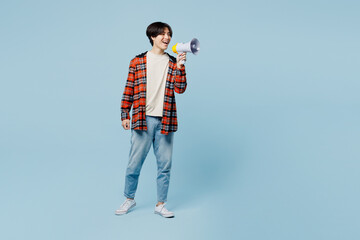 Full body young man of Asian ethnicity he wear red hoody casual clothes hold in hand megaphone scream announces discounts sale Hurry up isolated on plain light blue cyan background. Lifestyle concept