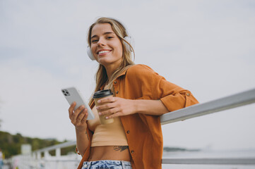Close up young woman wears orange shirt beige top casual clothes listen music in headphones use...