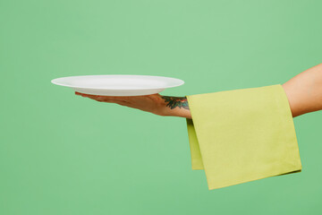 Close up cropped female hold in hand empty plate yellow towel with free space isolated on pastel plain light green color wall background studio. Cooking food concept. Copy space advertising mock up.