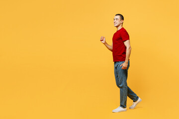 Full body side profile view smiling happy cheerful young middle eastern man he wear red t-shirt casual clothes walk go isolated on plain yellow orange background studio portrait. Lifestyle concept.