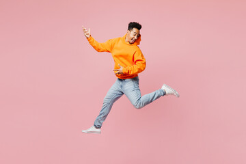 Fototapeta na wymiar Full body expressive happy young man of African American ethnicity wear yellow hoody casual clothes jump high play air guitar isolated on plain pastel light pink background studio. Lifestyle concept.