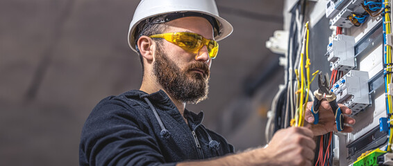 A male electrician works in a switchboard with an electrical connecting cable.