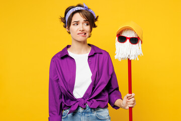 Young dissatisfied sad woman wear purple shirt casual clothes do housework tidy up hold in hand mop...