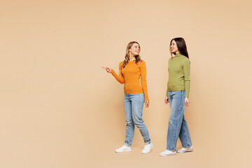 Full body young friend two women they wear orange green shirt casual clothes together walk go point index finger aside on area isolated on plain pastel light beige background studio Lifestyle concept
