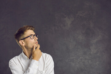 Serious millennial Caucasian man in glasses on black studio background look at blank empty copy space thinking making decision. Pensive young male consider sale deal or promotion offer. Copyspace.