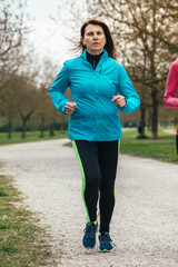 focused woman in blue jacket jogging in the park