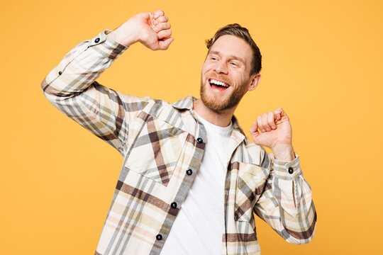 Young smiling happy satisfied positive Caucasian man he wear brown shirt casual clothes raise up hands dance look aside isolated on plain yellow orange background studio portrait. Lifestyle concept.