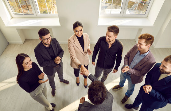 Team of people showing recognition to young business woman. Happy woman shaking hands with man while group of people are clapping. Professional success at work concept. High angle shot, from above