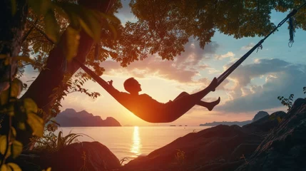 Schilderijen op glas A man enjoys calm, lies in a hammock on the background of the ocean and sunset. © Ruslan Gilmanshin