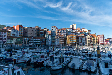 Fototapeta na wymiar Panoramic view of the touristic Basque coastal town of Bermeo, in front of a small harbour full of boats and their colourful facades on a sunny day.