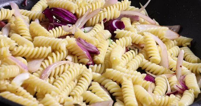 Frying sauteing fusilli pasta macaroni in non stick pan with olive oil sliced onion shallot