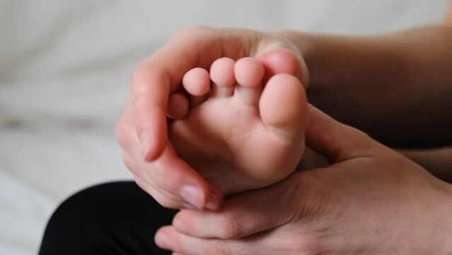 The mother is doing massage of foot for her child. Counting the toes. Mom gently stroking the baby. Tactile contact. Gentle relationship. Love atmosphere. Happy moments of motherhood and childhood