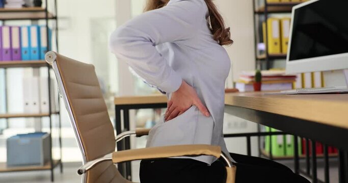 Woman with backache stretches waist sitting at desk in office