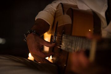 Close-up of a Spanish person playing the classical guitar. The man is illuminated by candlelight.