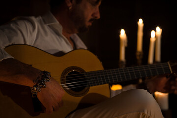 Obraz premium Spanish person playing the classical guitar. The man is illuminated by candlelight.
