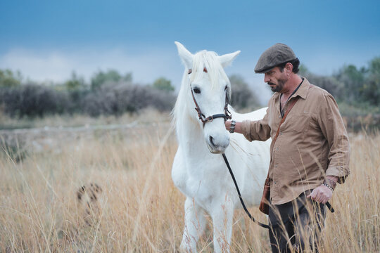 Spanish cattleman in beret walking his white horse in a field of tall grass with copy space.