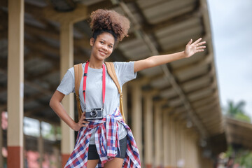Young Asian African woman traveler with backpack in the railway train station, traveler girl walking stand sit waiting take a picture on railway platform train station. High quality photo - obrazy, fototapety, plakaty
