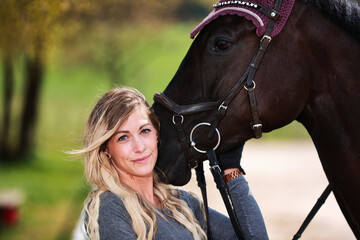 Young woman with long hair and blonde streaks, stands portraits with her horse.