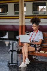 Asian African female tourist traveler holding mobile phone smart phone sitting at train station,...