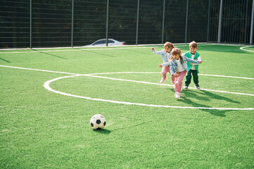 Running with ball. Kids are having fun on the green soccer field together