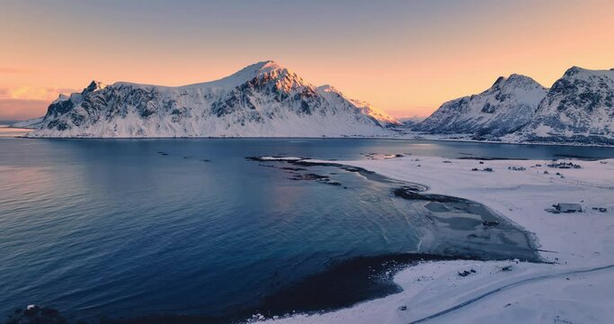 Winter landscape with snow covered mountains peaks, rocky coastline and scenic sunset over Uttakleiv Beach, Lofoten Islands, Norway aerial 4K video
