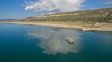 Clouds reflected on the lake and a boat travelling on the lake. Forest and mountain in the...