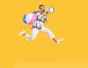 Excited man jumping with inflatable sea ball and screaming into megaphone. Full length shot of happy young man wearing sunglasses and summer casual clothes having fun on isolated studio background