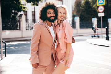 Obraz premium Beautiful fashion woman and her handsome elegant boyfriend in beige suit. Sexy blond model in summer suit clothes. Fashionable smiling couple posing in street Europe. Brutal man and female outdoors