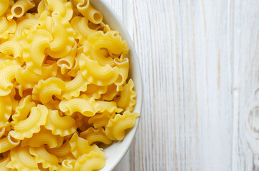 Raw Creste Di Gallo pasta in a gray bowl on a white wooden board. Rooster comb. The concept of traditional Italian food. Horizontal orientation. Copy space. Top view
