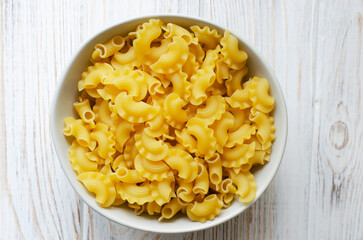 Raw Creste Di Gallo pasta in a gray bowl on a white wooden board. Rooster comb. The concept of...