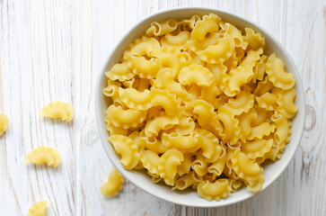 Raw Creste Di Gallo pasta in a gray bowl on a white wooden board. Rooster comb. The concept of traditional Italian food. Horizontal orientation. Copy space. Top view