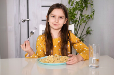 Happy girl eating pasta. Child eats his lunch in kitchen at table. Selective focus