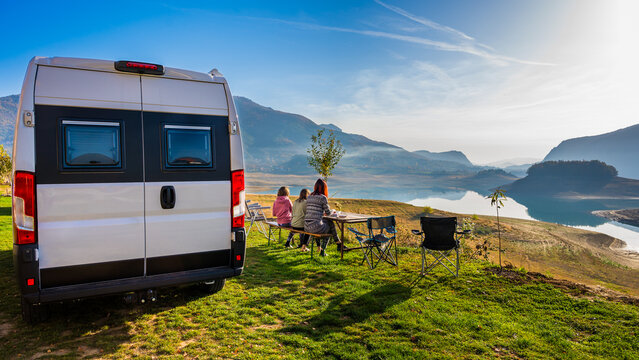 Campervan, Motorhome RV parked next to the lake or river in Bosnia and Herzegovina. Family with camper van or motor home eating breakfast on an active family vacation on a road trip to Ramsko lake.