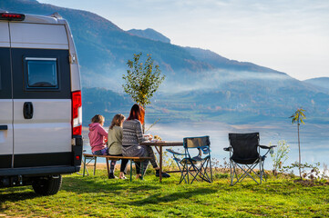 Campervan, Motorhome RV parked next to the lake or river in Bosnia and Herzegovina. Family with camper van or motor home eating breakfast on an active family vacation on a road trip to Ramsko lake.