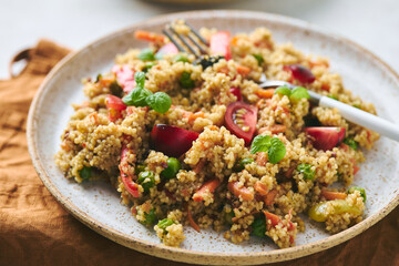 Vegan warm salad made with couscous, tomatoes, green beans, mint, roasted carrots and sweet peppers. Couscous with vegetables in bowl on light background. Variation of Tabbouleh Salad.