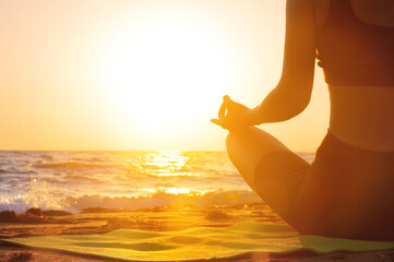 Close-up Yoga woman meditating at serene sunset or sunrise on the beach. The girl relaxes in the lotus position. Fingers folded in mudras.