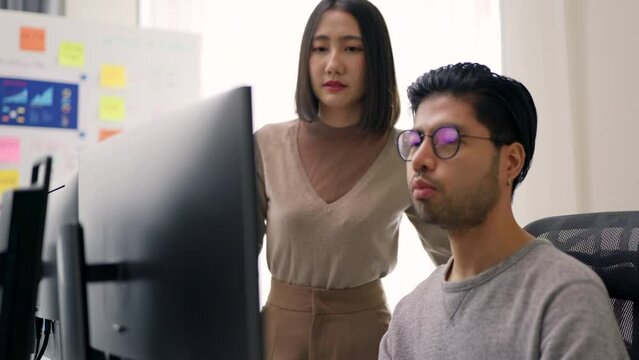 A focused male programmer and his female colleague collaborate on critical code development at their shared workstation in a modern office.