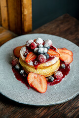 Homemade fluffy pancake with fruits and cream on the top, on a wooden table. Top view