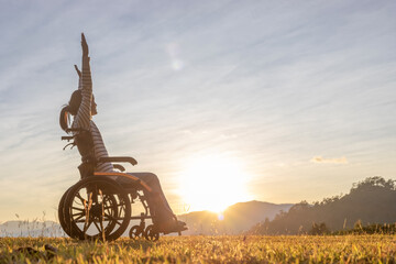 Silhouette happy girl raised hands in wheelchair looking sunset mountain background.