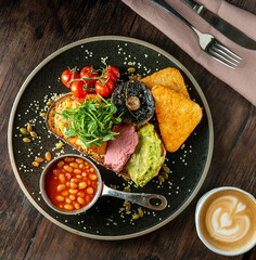 English Breakfast served on a black ceramic plate. Wooden table. Top view