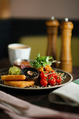 English Breakfast served on a black ceramic plate. Wooden table. Side view