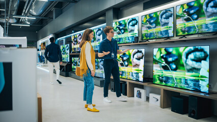 Beautiful Female Client Having a Conversation with Retail Home Electronics Shop Consultant. Young Woman is Shopping for a Modern TV Set. Customer Looking for a New Television in Department Store