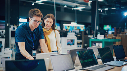 Attractive Woman Discusses Laptop Options with Home Electronics Store Sales Associate. Young...
