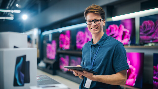 Portrait of an Organized Handsome Assistant in Home Electronics Store Optimizing Workflows with Tablet Computer. Young Happy Team Member Looking at Camera and Smiling