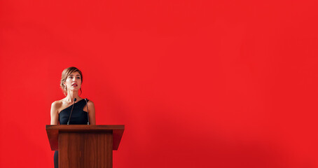 femme en robe de soirée qui fait un discours derrière un pupitre - fond rouge - obrazy, fototapety, plakaty