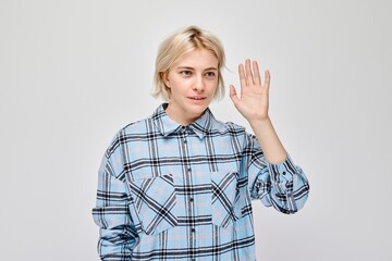 Blonde woman in plaid shirt gesturing hello with her hand, isolated on a light background.