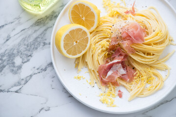 Plate of spaghetti with prosciutto and lemon zest, horizontal shot on a white marble background, middle closeup