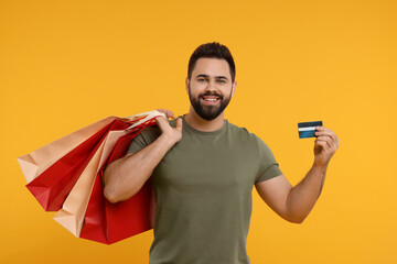 Smiling man with many paper shopping bags and credit card on orange background