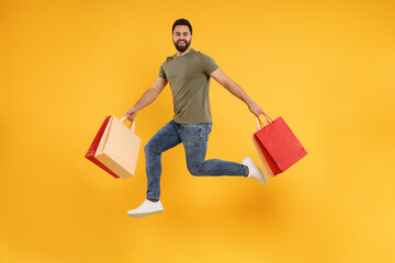 Happy man with many paper shopping bags jumping on orange background