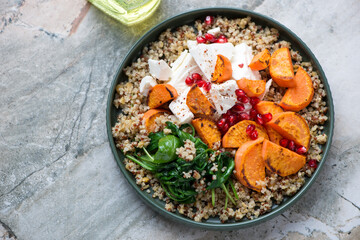 Quinoa with roasted sweet potato, feta, pomegranate and wilted spinach, horizontal shot on a grey granite background, elevated view